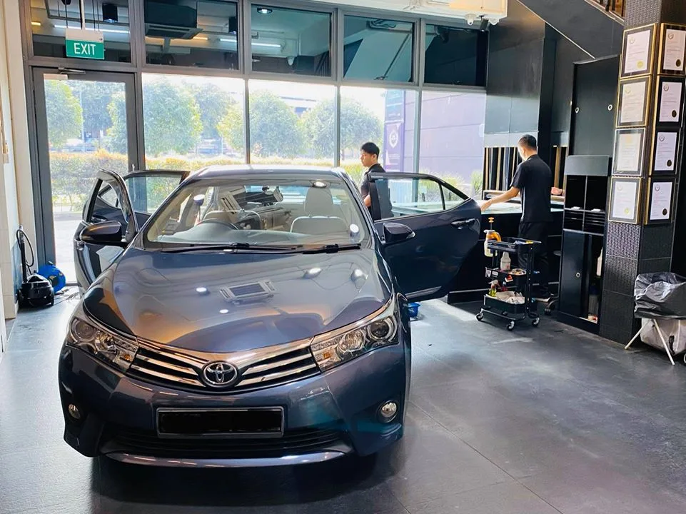 Blue-grey Toyota Altis front view with installers at work inside Infratint Singapore