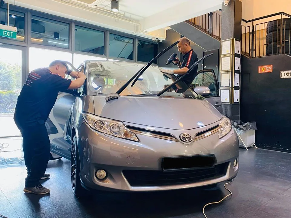 Technicians fitting windscreen film to a silver Toyota Previa at Infratint Singapore