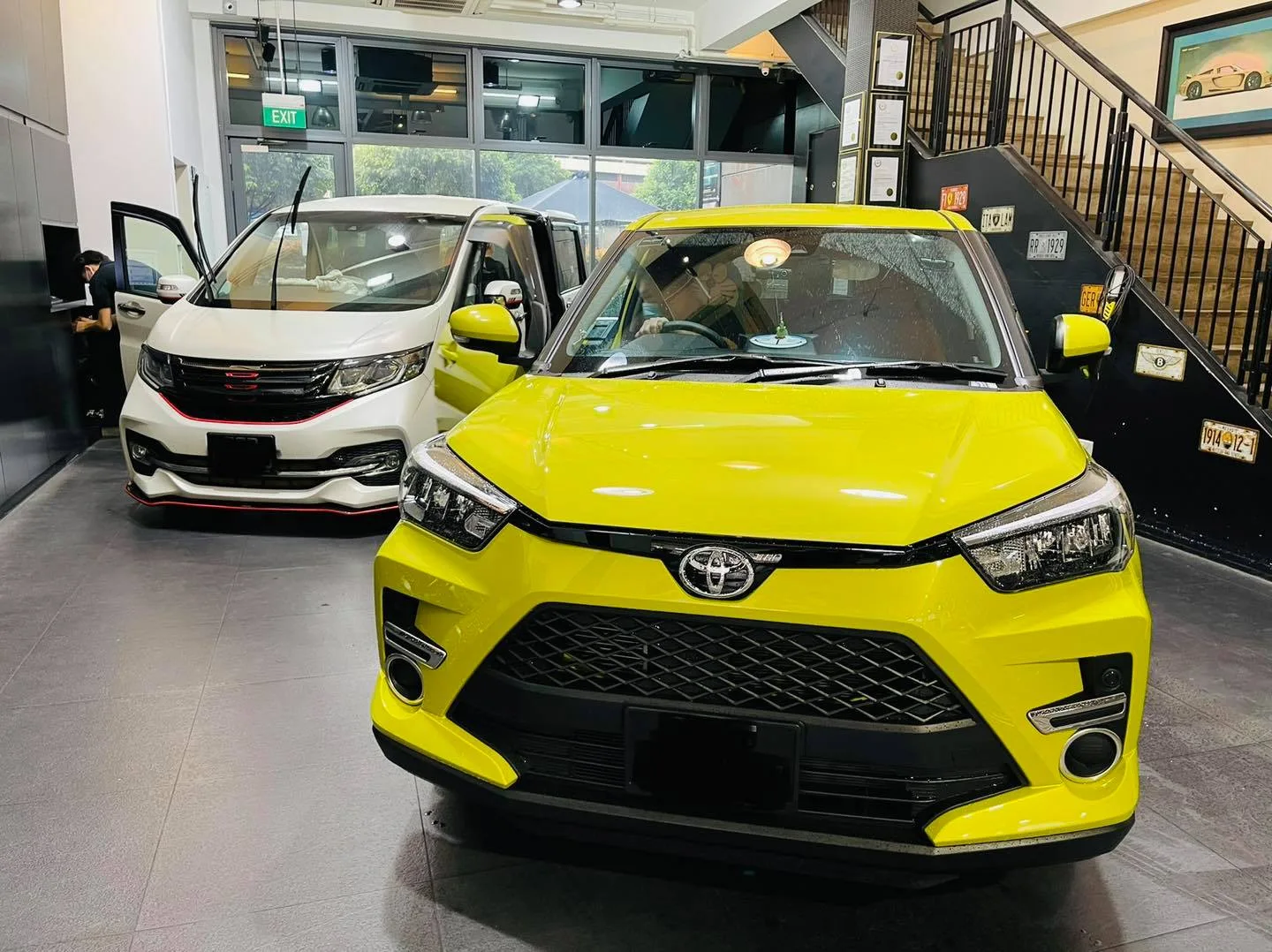 Yellow Toyota Raize SUV and a white Honda MPV inside the Infratint Singapore showroom