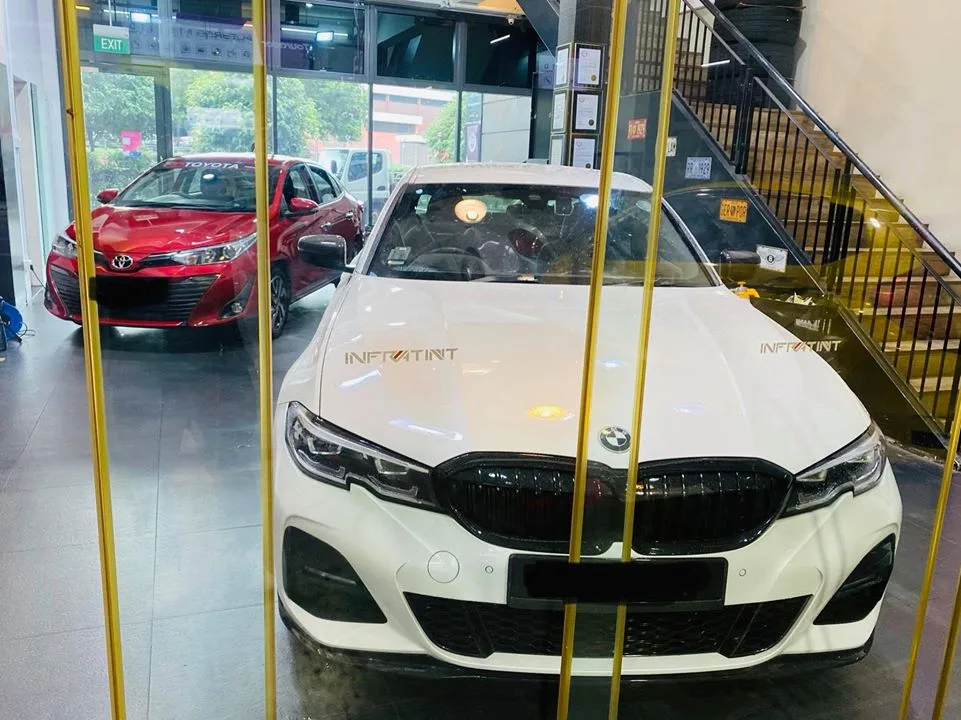 White BMW sedan with Infratint bonnet decal beside a red Toyota at Infratint Singapore