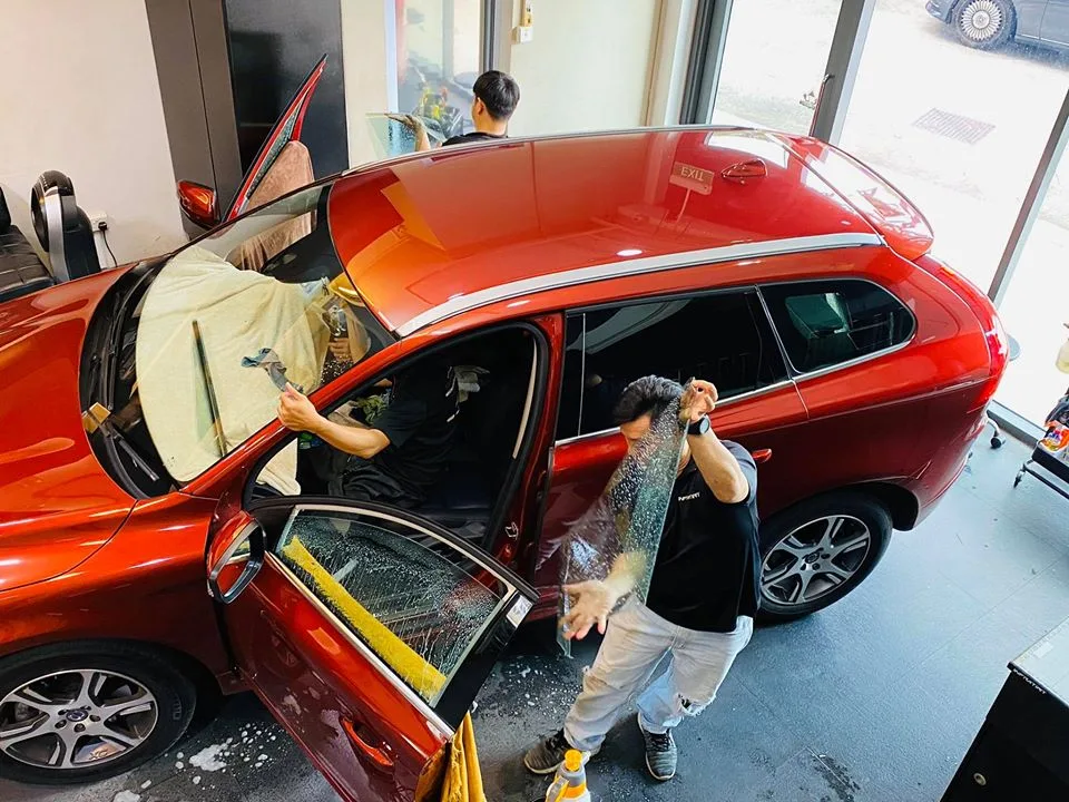 Two installers fitting window film to a copper Volvo XC60 at Infratint Singapore